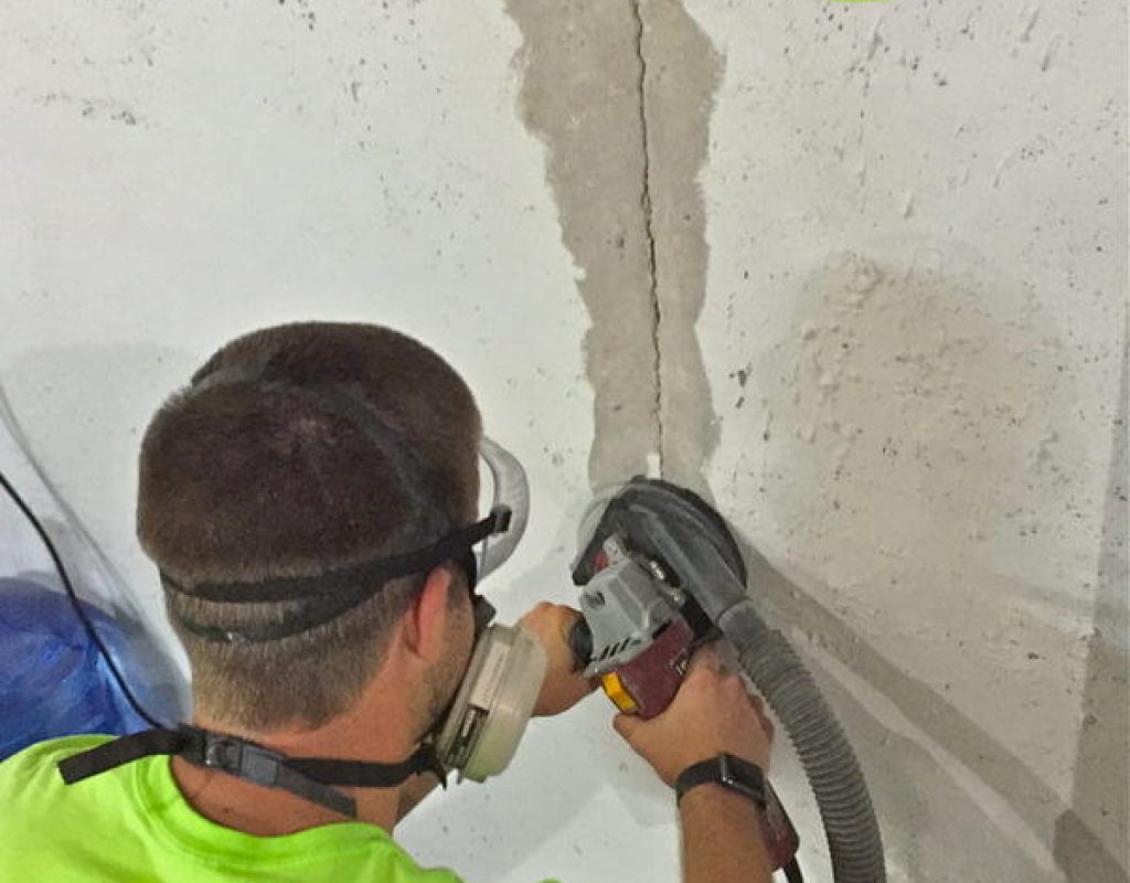 A Sealed LLC technician grinding down a layer of sealant along a basement retaining wall